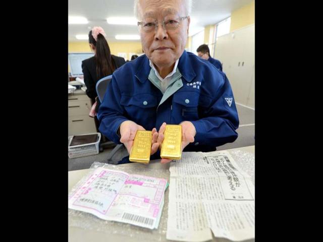Kunio-Sunow-president-of-the-Ishinomaki-Fish-Market-shows-off-two-slabs-of-gold-each-weighing-one-kilogram-2-2-pounds-as-well-as-the-parcel-s-invoice-bottom-L-and-an-enclosed-magazine-article-bottom-R-at-his-office-in-Ishinomaki-Miyagi-prefecture-AFP