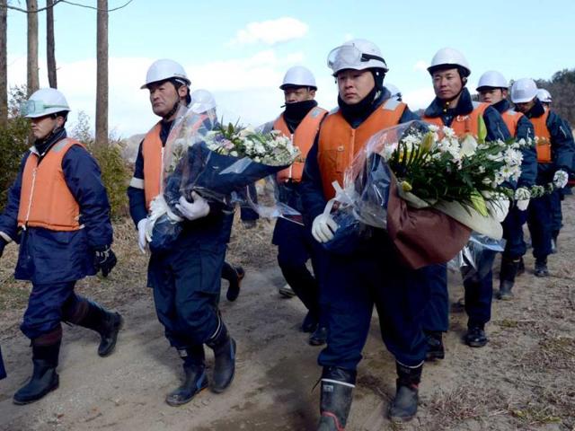 Police officers carry bouquets of flowers as they return to recommence their search misson for tsunami victims at the mud-covered riverside field near the Okawa elementary school in Ishinomaki city, Miyagi prefecture.AFP Photo