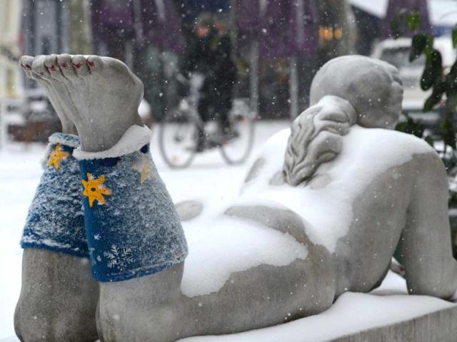 A cyclist passes a snow-covered sculpture with knitted cuffs in Frankfurt Germany. (AP)