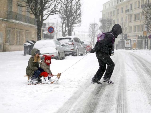 Children cross a snowy road on a sledge, in Caen, northwestern France, during a heavy snow storm on France. (AFP)