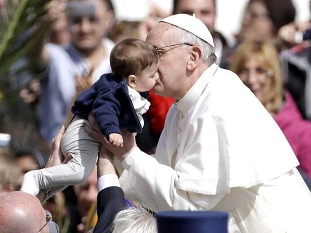 Pope Francis kisses a child as he leaves after celebrating his first Palm Sunday Mass, in St. Peter's Square. AP