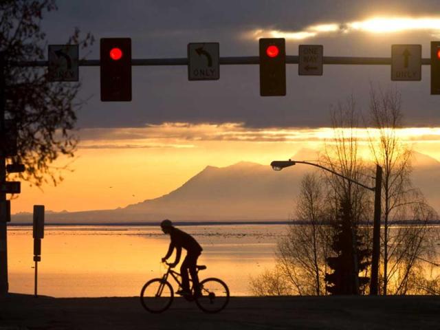 A cyclist heads south on L Street in downtown Anchorage, Alaska as the late-day sun peeks through the clouds over Cook Inlet. AP photo