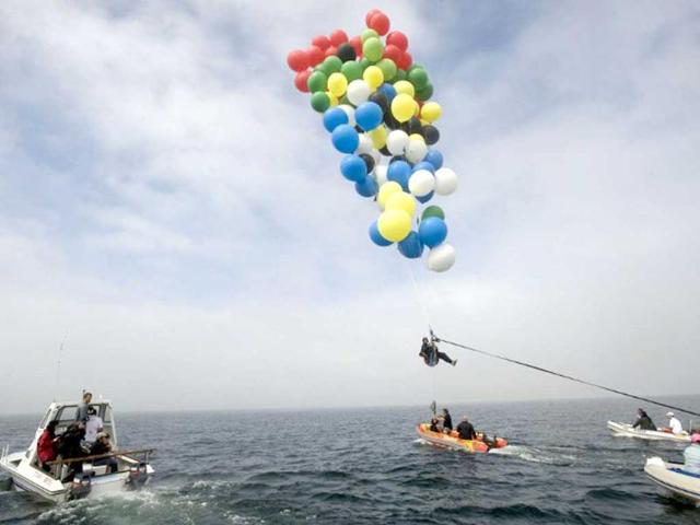 Matt Silver-Vallance flies above Table Bay, with some of his support crew in boats from Nelson Mandela's apartheid island prison using helium-filled giant party balloons in Cape Town. AFP