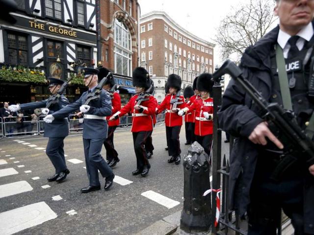 An armed police officer stands guard as military personnel march past ahead of the ceremonial funeral procession for former British Prime Minister Margaret Thatcher in London. AP Photo