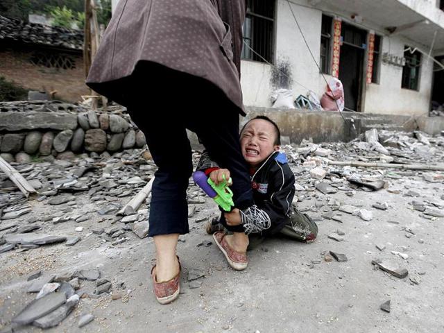 A boy holds his mother's leg as he cries in front of their damaged house after a strong 6.6 magnitude earthquake at Longmen village, Lushan county in Ya'an, Sichuan provinc, in China. Reuters