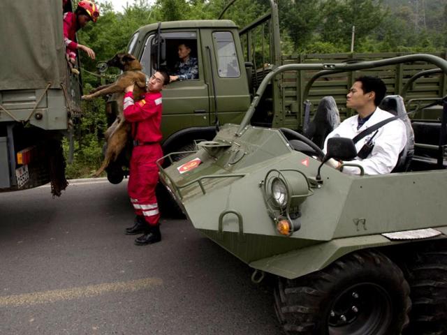 A rescue worker helps a sniffer dog down from a truck along a road leading out of the county seat of Lushan in southwestern China's Sichuan province. AP