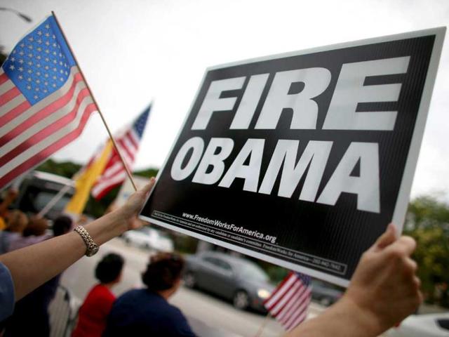 A protesters holds a sign reading, "Fire Obama", as she waits for President Barack Obama's motorcade to drive past in Miami Beach, Florida. President Obama traveled to the Miami area to attend private fundraising events for the Democratic National Committee. (AFP)