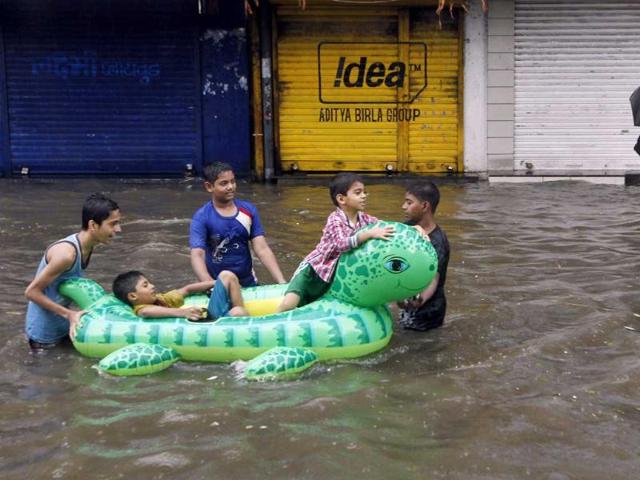 Children enjoy the rain floating on an inflated tube on a flooded street after heavy monsoon rains in Mumbai. AP