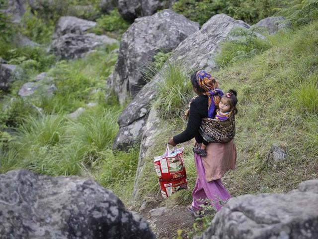 A woman carrying a baby on her back walks down a hill during a rescue operation at Govindghat in Uttarakhand. (Reuters)