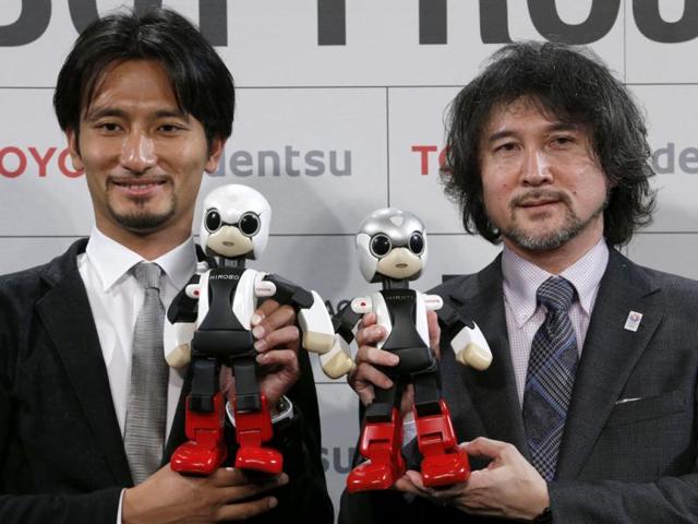 Humanoid communication robots, Kirobo, bottom left, and Mirata, bottom right, are held by Tomotaka Takahashi, left, CEO of Robo Garage Co. and project associate professor from the University of Tokyo, and Fuminori Kataoka, project general manager from Toyota Motor Corp., during a press unveiling in Tokyo. (AP Photo)