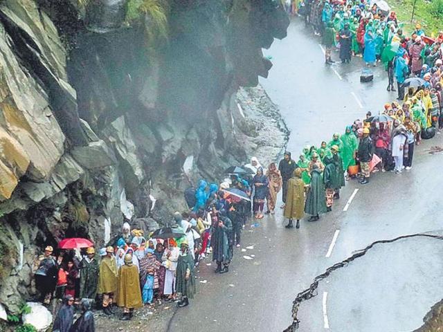 Security personnel supervise people as they stand on a flood-damaged road. (Army)
