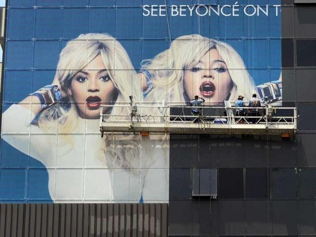 Workers cover glass windows of a highrise building in Hollywood with advertising for the current tour by popstar Beyonce in Hollywood, California. AFP