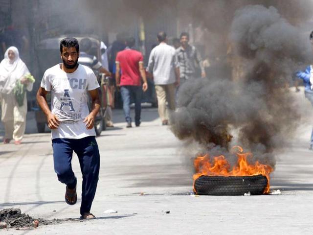 Kashmiris run past a burning tyre during a protest against the killing of villagers by Border Security Force soldiers in Srinagar. (HT Photo/Waseem Andrabi)