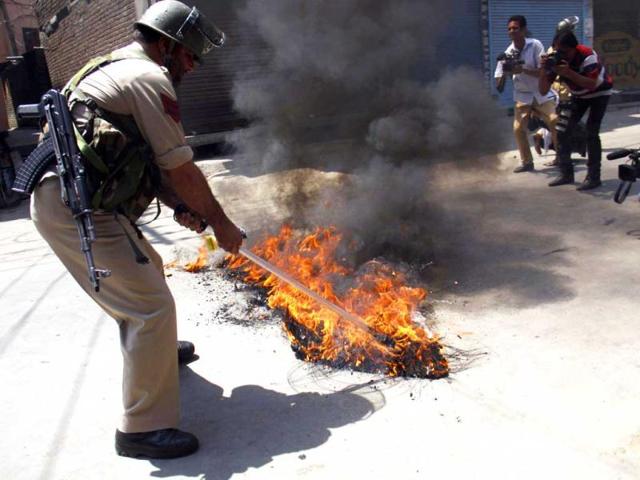 A policeman removing a burning tyre during a protest against the killing of locals by Border Security Force soldiers in Srinagar. (HT Photo/Waseem Andrabi)