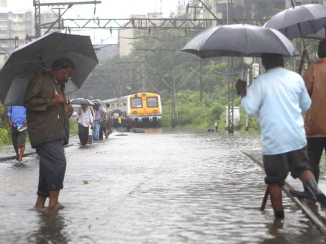 Mumbaikars walk along flooded railroad tracks during heavy rain showers near Chunabhatti in Mumbai, India. (HT Photo)