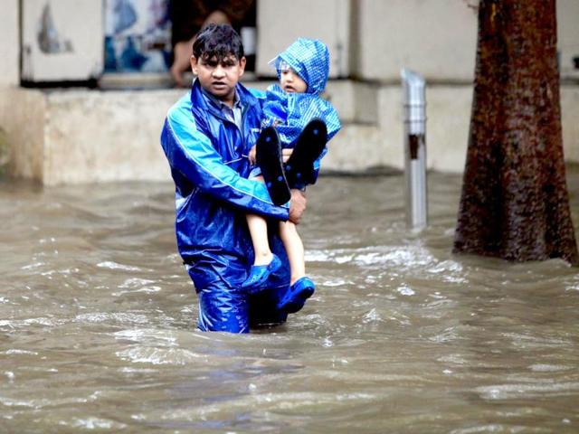 A man carries a child through a flooded street during rain showers in Mumbai. (PTI Photo)