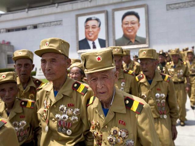 North Korean veterans of the Korean War walk under portraits of the late leaders Kim Il Sung and Kim Jong Il at the end of a mass military parade. (AP Photo)