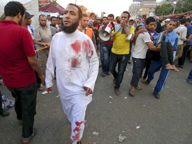A blood-stained supporter of Egypt's ousted President Mohammed Morsi walks as others carry an injured man to a field hospital following clashes with security forces at Nasr City, where pro-Morsi protesters have held a weeks-long sit-in, in Cairo, Egypt, Saturday, July 27, 2013. (AP Photo)