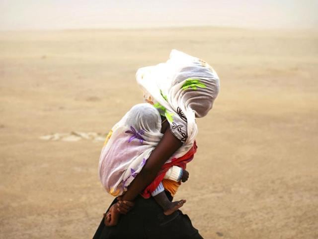 A woman carrying her baby and wrapped with a shawl walks through a sandstorm in Timbuktu. (Reuters Photo)