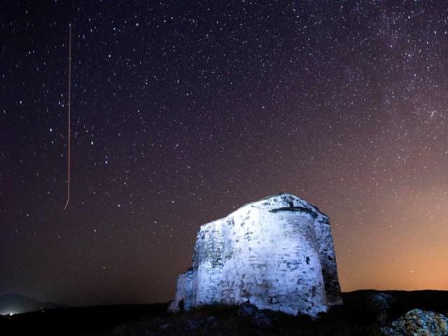 A long exposure image showing a Perseids meteor (L) streaking across the night sky over St. Ioan medieval church near the village of Potsurnentsi. (AFP Photo)