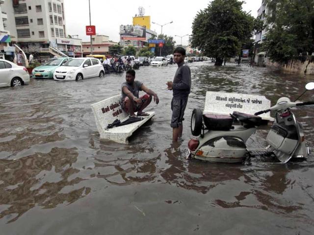 A man sits on a stone bench as motorists drive past a flooded street after heavy rains in Ahmadabad. (AP Photo)