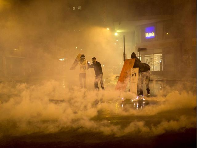 Demonstrators with their faces covered take cover from tear gas fired by riot police in Rio de Janeiro, Brazil. (AP Photo)