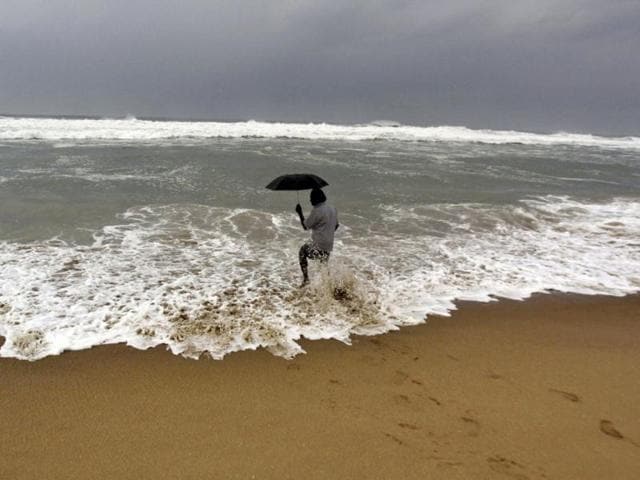 A man holds on to his umbrella as he fishes in high tide waves at Gopalpur beach, in Ganjam district, Odisha.(AP Photo)