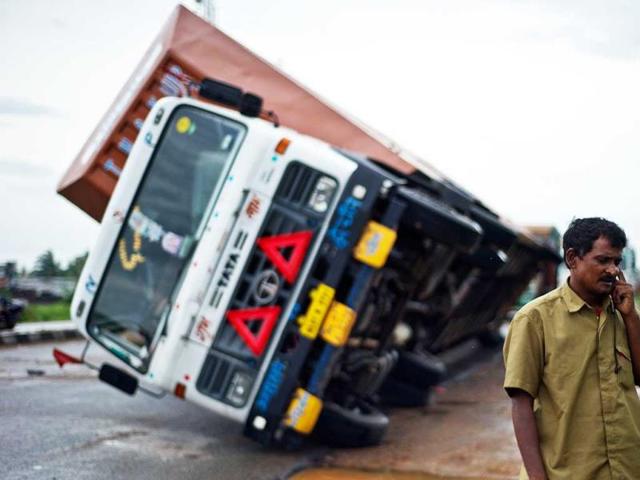 A truck driver speaks on his phone after his truck carrying Toyota cars was overturned by strong winds Andhra Pradesh-Odisha National Highway. (AFP Photo)