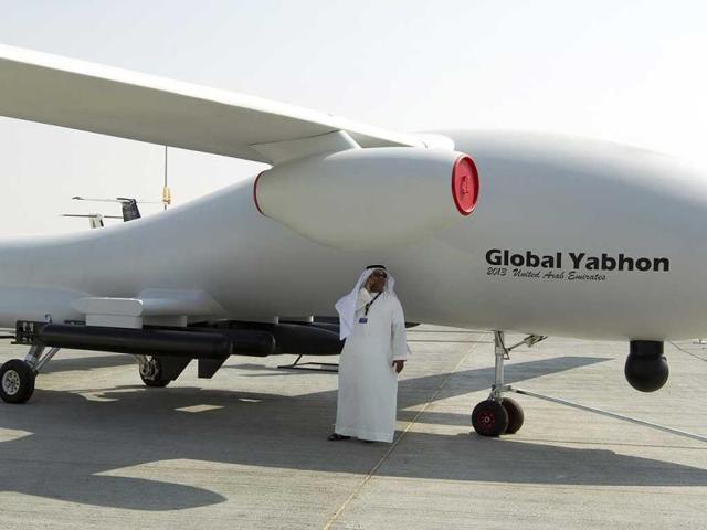 A visitor speaks on his phone in the shade of unmanned drone during the Dubai Airshow. (Reuters Photo)