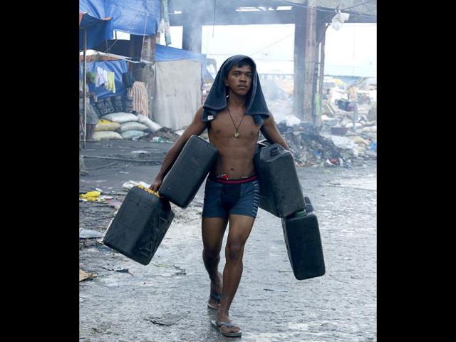 A typhoon survivor carries plastic containers to fetch water from a broken pipe after typhoon Haiyan battered Tacloban city nearly two weeks ago in central Philippines. (Reuters)
