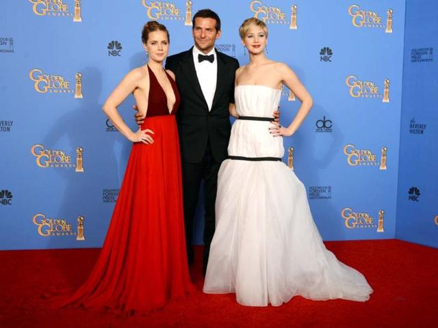 Both Amy Adams, in her sleeveless burgundy dress, and Jennifer Lawrence, in her white dress covered with two black bands (why?), failed to fire fashion critics' imagination. Bradley Cooper poses with the two beauties.