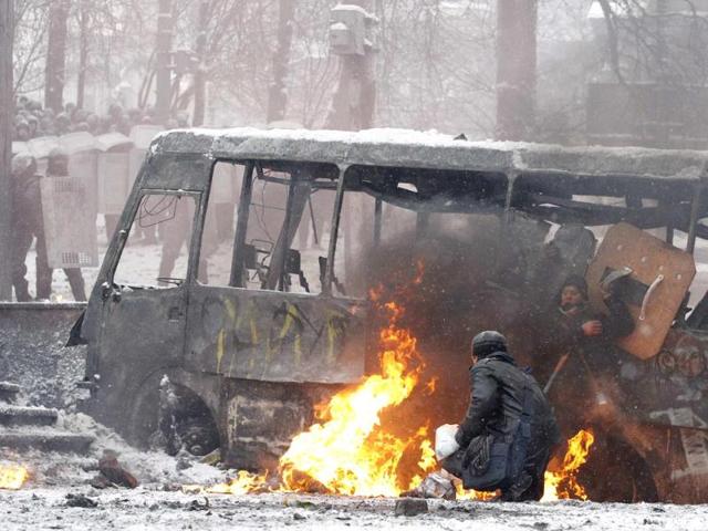 Pro-European protesters take cover behind a burnt bus during clashes with riot police in Kiev. (Reuters Photo)