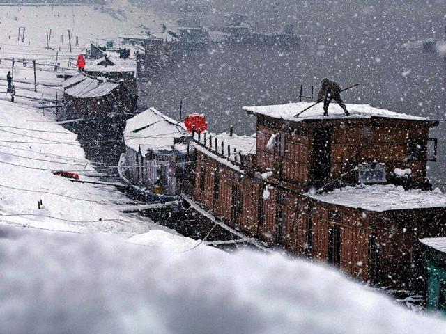 A man clears snow from the roof of his houseboat during heavy snowfall at river Jehlum in Srinagar. Kashmir valley experienced fresh snowfall prompting authorities to suspend traffic on Srinagar-Jammu national highway and air service. (PTI photo)