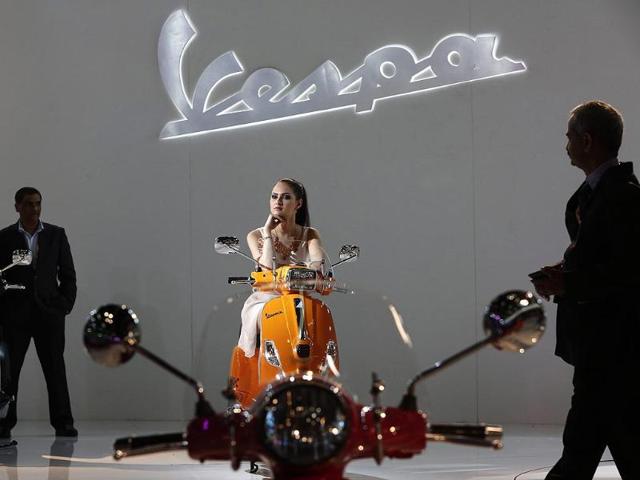The presence of models brings glam to the event which is all about jazzy cars and cool bikes. A model poses with a Vespa 946 scooter as visitors walk around during the 12th Auto Expo 2014 in Greater Noida, on the outskirts of New Delhi. (Reuters)