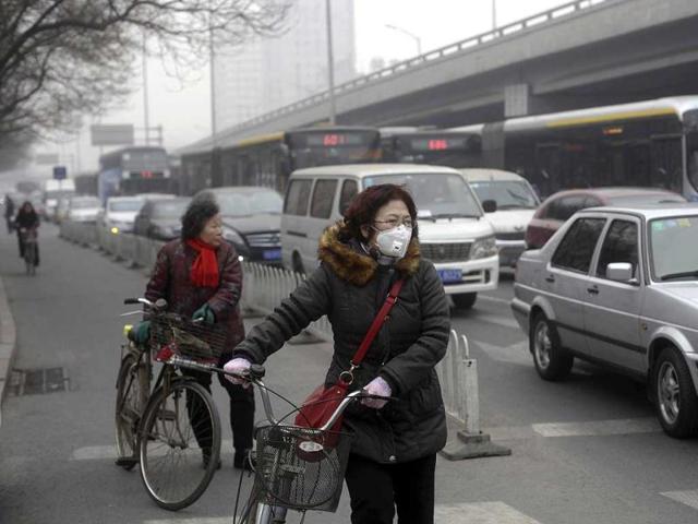 A woman (C) wearing a mask stands besides her bicycle as vehicles stop at a traffic junction on a busy street amid thick haze in Beijing February 25, 2014. Reuters/Barry Huang