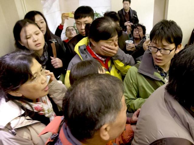 A woman, center, surrounded by media covers her mouth on her arrival at a hotel which is prepared for relatives or friends of passengers aboard a missing airline, in Beijing. (AP Photo)