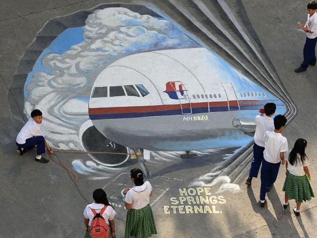 Students stand next to a giant mural featuring missing Malaysia Airlines flight MH370 displayed on the grounds of their school in Manila's financial district of Makati. (AFP Photo)
