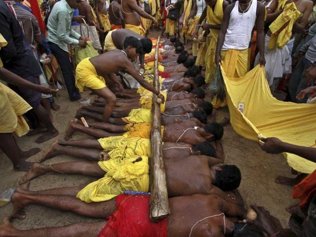 A man breaks coconuts on a wooden pole placed above villagers who lay on hot sand at the annual Danda festival in Odisha. (AP Photo)
