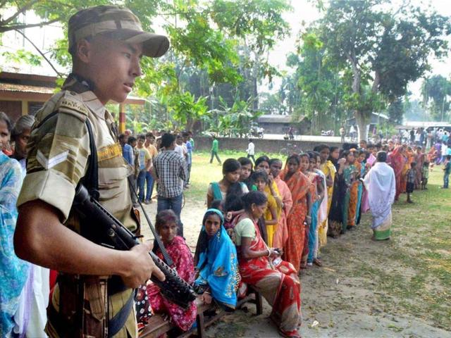 Security guard keeping vigil as women queue up to cast their vote, outside a polling center at Koliabor in Nagaon district of Assam. (PTI Photo)