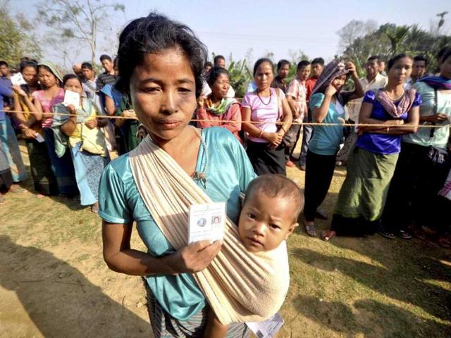 A woman voter carries her kid as others wait to cast votes for Tripura West Lok Sabha polls outside a polling station in Dhamcherra. (PTI photo)
