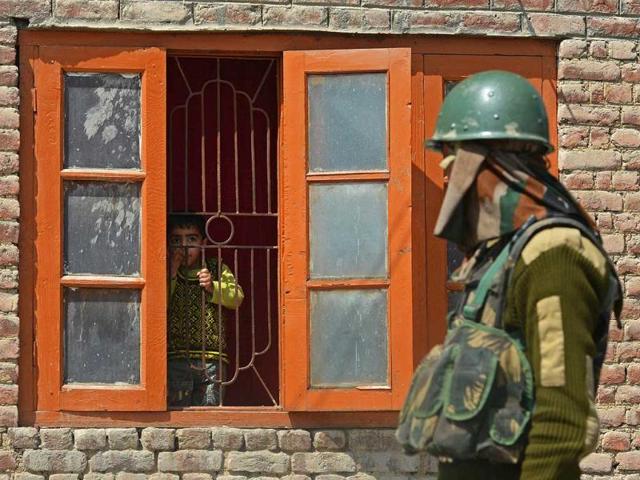 A Kashmiri child looks out a window as an Indian paramilitary trooper walks past near the vicinity of a gunfight between suspected militants and Indian troops in the outskirts of Srinagar. (AFP Photo)