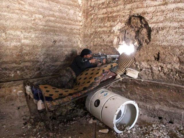 A rebel fighter aims his rifle from behind a wall as he holds a position in the outskirts of the village Papoulan, in Idlib province. (AFP Photo)
