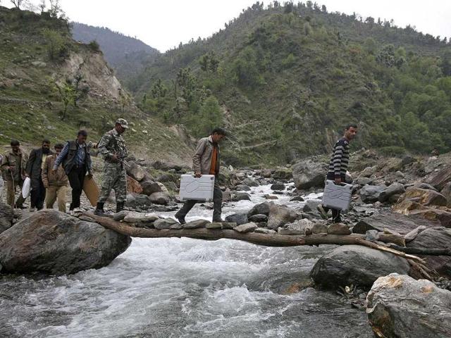EC staff carry electronic voting machines (EVM) across a water channel on their way to polling stations ahead of the fifth phase of LS elections in Assar, Jammu. (Reuters photo)