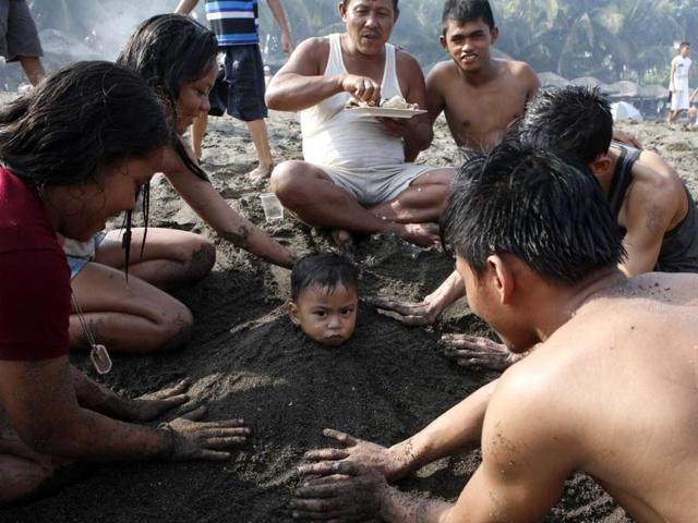 A family helps bury a boy in sand at a beach to celebrate Easter Sunday, near Manila Bay in Cavite. (Reuters Photo)