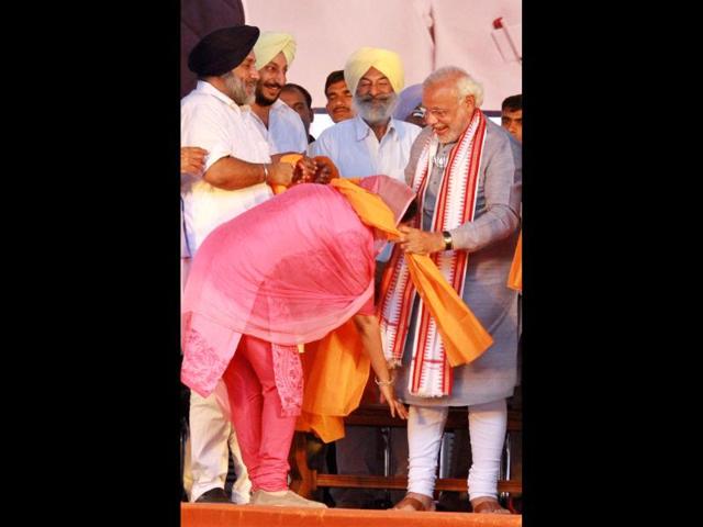 SAD candidate Harsimrat Kaur Badal touches the feet of BJP’s PM candidate Narendra Modi during an election rally in Bathinda. (PTI Photo)