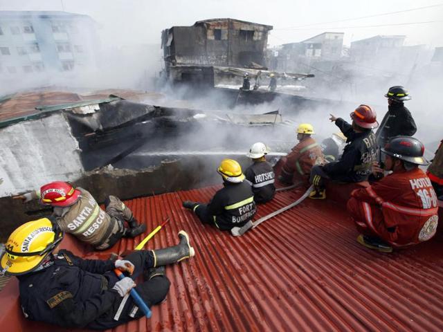 Firemen keep watch on a rooftop next to an apartment building on fire to prevent it from spreading, in Manila. (Reuters photo)
