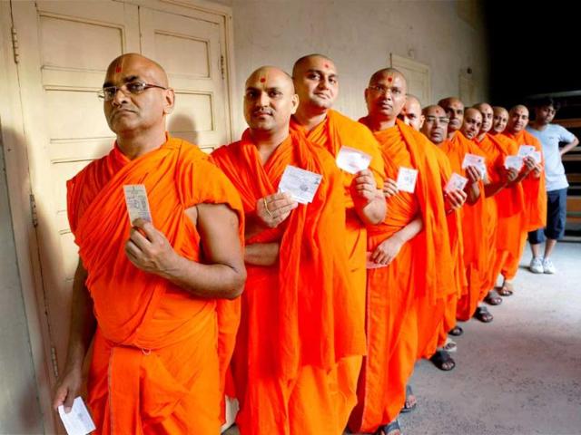 Swaminarayan Temple priests show their ID cards as they wait in a queue to cast their vote during Lok Sabha elections in Ahmedabad. (PTI Photo)