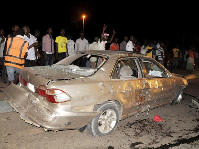 People-gather-near-the-damaged-car-following-a-bomb-explosion-in-Abuja-Nigeria-A-car-bomb-exploded-on-a-busy-road-in-Nigeria-s-capital-days-before-the-city-is-to-host-a-major-international-economic-forum-AP-Photo