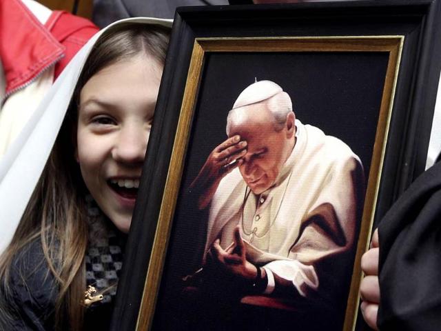 A girl smiles next to a picture of John Paul II as Pope Francis visits a Polish community at St. Stanislaw church in Rome. (Reuters)