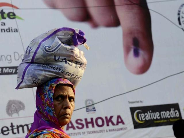 A pedestrian carries a bag over her head as she walks past a banner urging people to vote in Varanasi . (AFP)